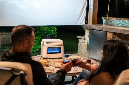 Couple toasting with drinks around a stone table with snacks and a modern outdoor heater under a white screen