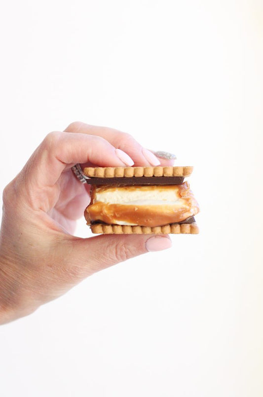 Hand holding a caramel and cream ice cream sandwich with chocolate and biscuit layers