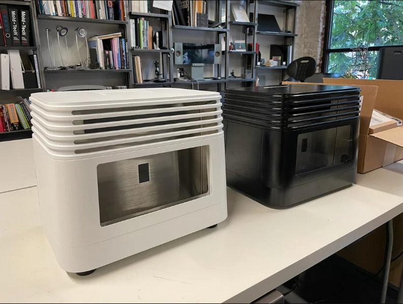 White and black modern air purifiers on a white table in a bright office with shelves and windows