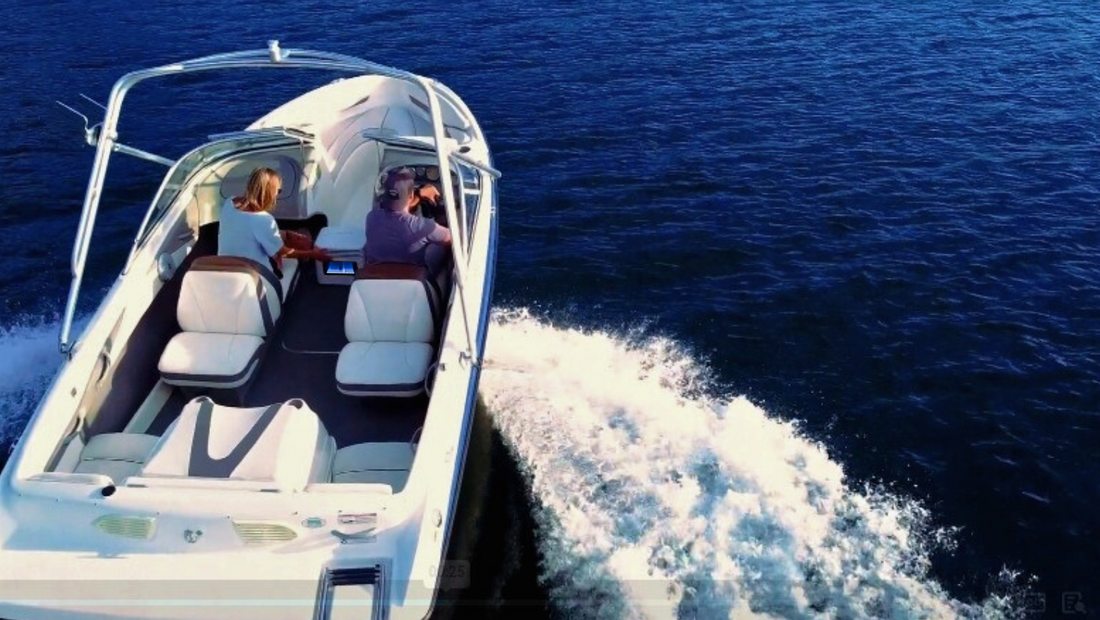 Two people driving a white motorboat on deep blue water with visible wake trail