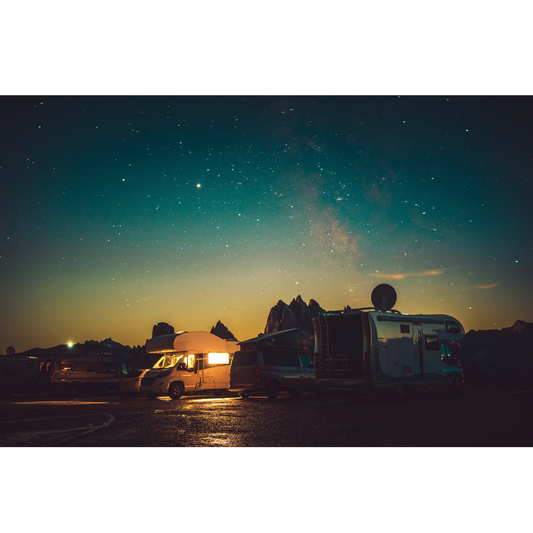 Nighttime campsite with illuminated RVs and starry sky against mountain silhouette
