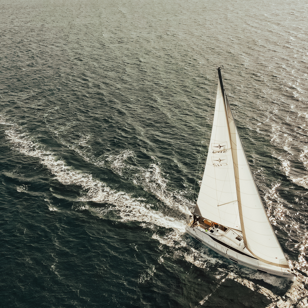 A white sailboat gliding on dark blue ocean waters with sails fully open under sunlight
