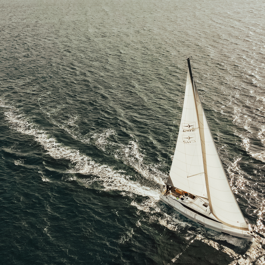 A white sailboat gliding on dark blue ocean waters with sails fully open under sunlight