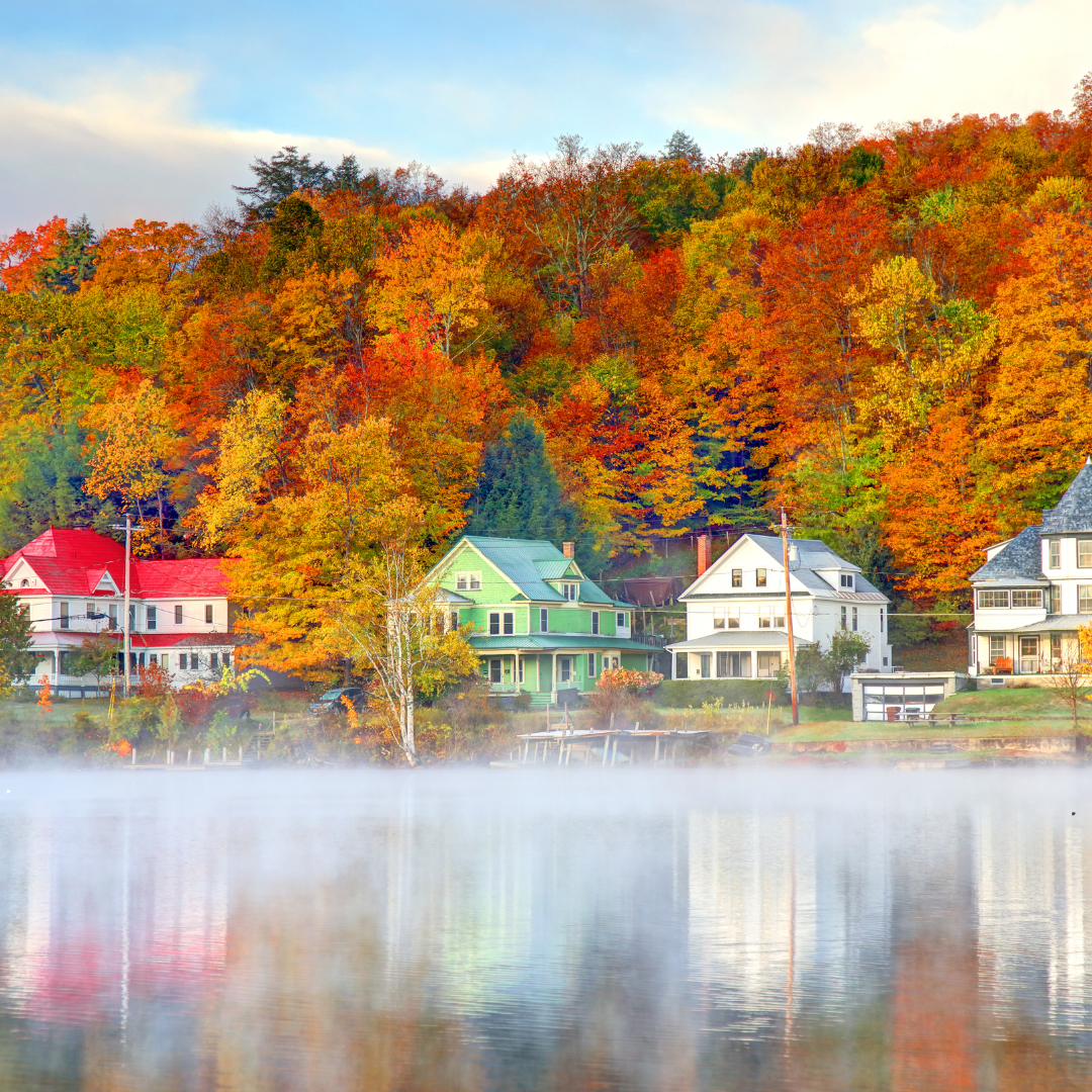 Colorful autumn trees behind lakeside houses with reflections and morning mist on water