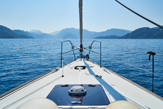 View from a sailboat deck sailing on calm blue sea with mountain landscape under clear sky