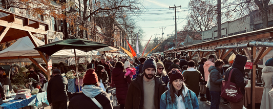 Crowded outdoor winter farmers market with people shopping and stalls under umbrellas and wooden canopies