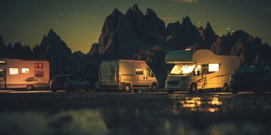 Night scene of RVs and camper vans parked near mountains with lights on under a starry sky