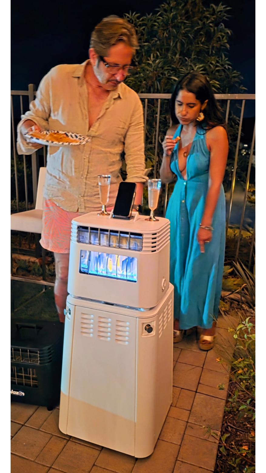 Two people standing next to a large electronic device on a patio at night.