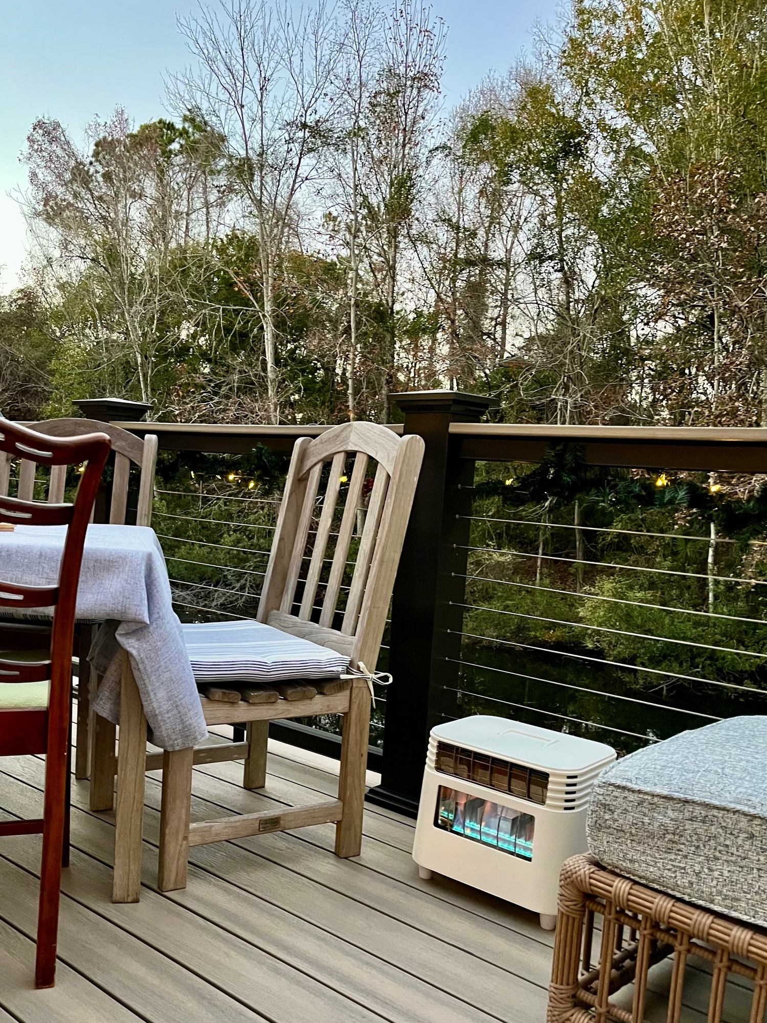 Outdoor deck with chairs, table, and gas grill on a wooden deck with trees in the background.