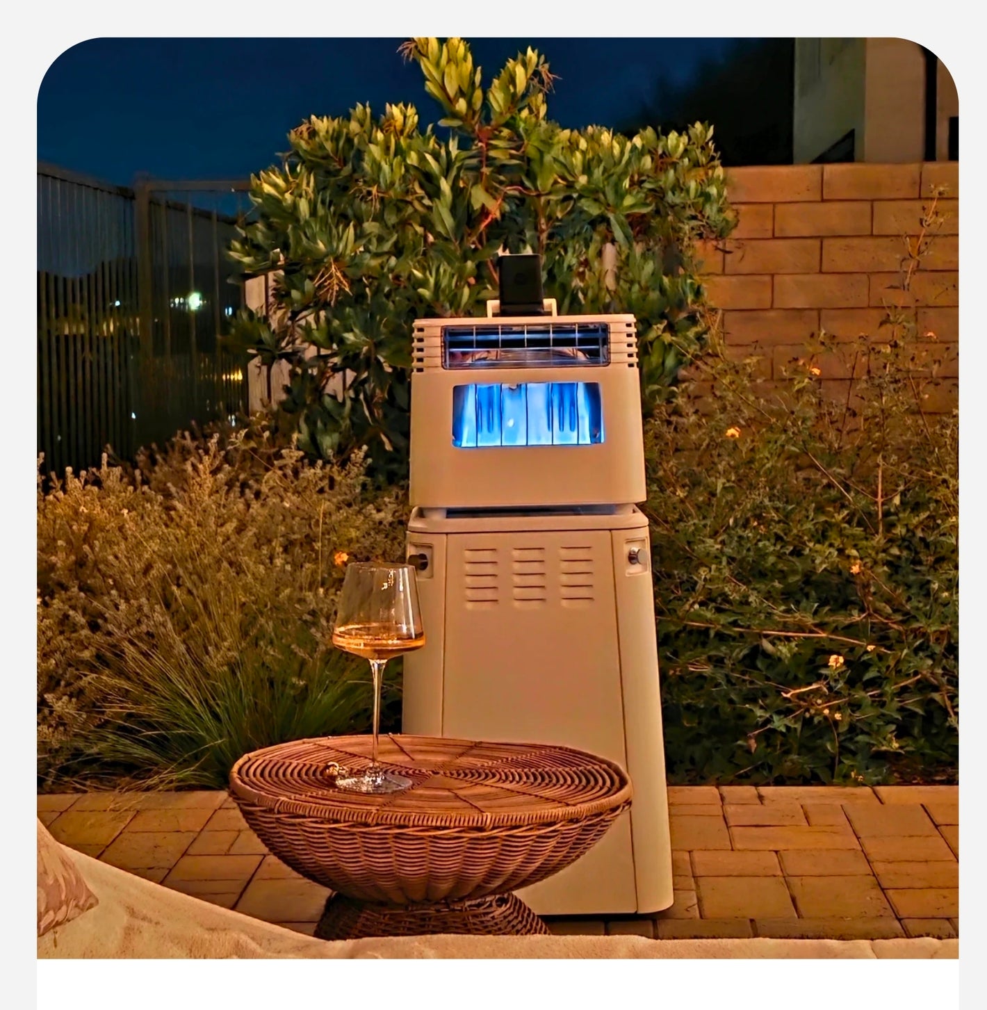 Outdoor patio heater with a glass of wine on a table in a garden setting.