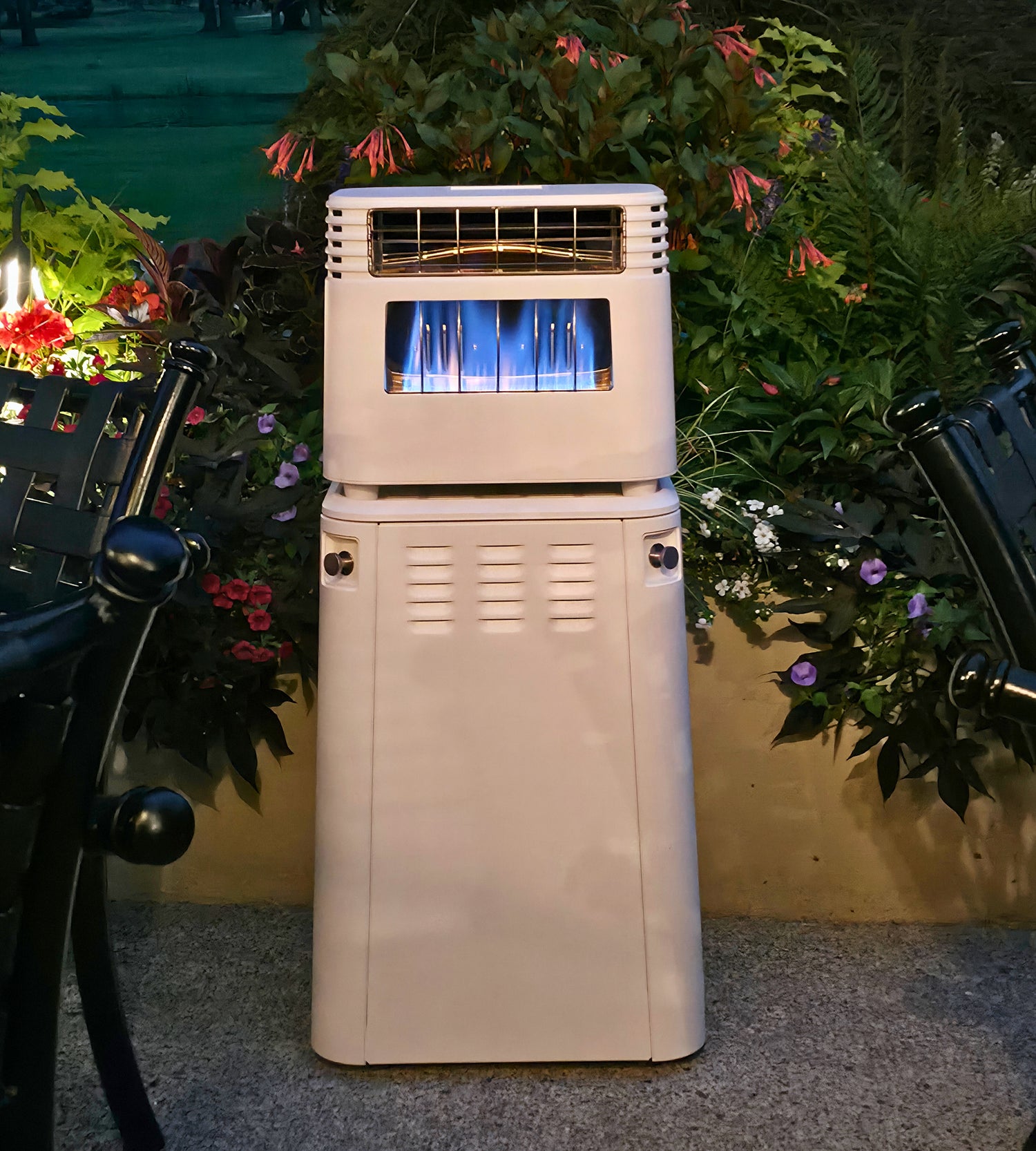 White outdoor patio heater with blue flames, surrounded by green plants and black chairs
